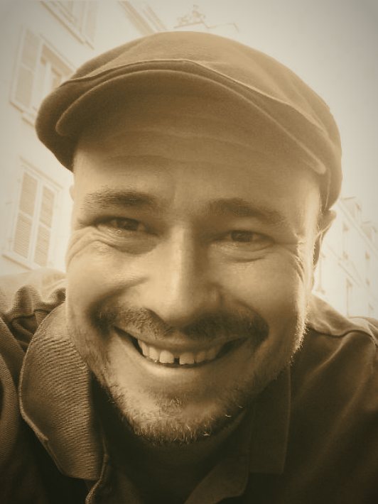 Portrait de François Petit, souriant, coiffé d’une casquette